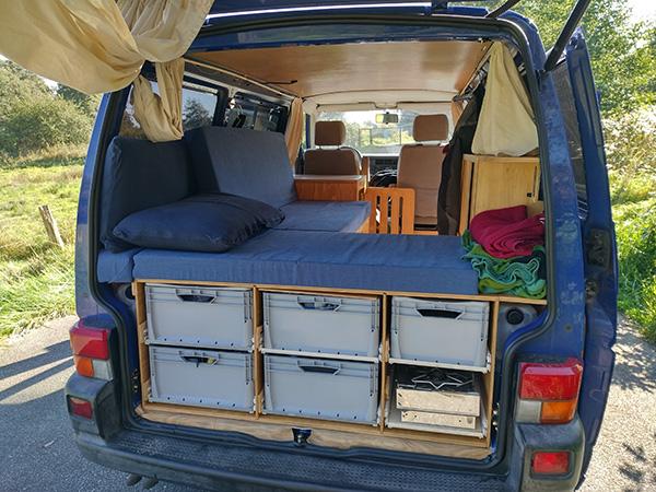 Interior view of Jo and Georg’s blue VW T4 van from triptovantasia, showing their minimalist bed setup and storage solutions during their vanlife journey.