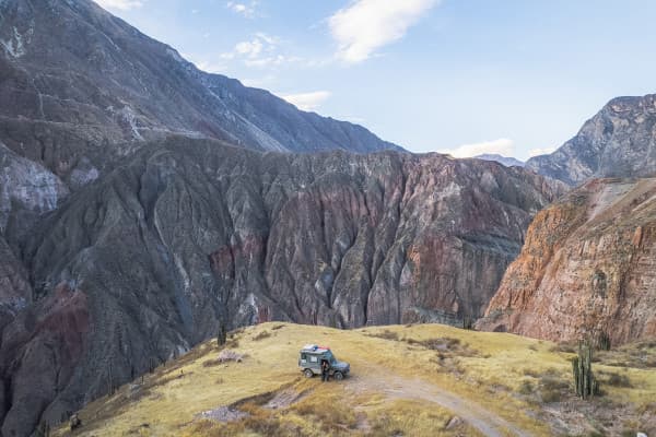 A Puch 230GE 4x4 offroad camper parked on a grassy plateau overlooking dramatic, multicolored cliffs and rugged mountains in the Cotahuasi Canyon in Peru.