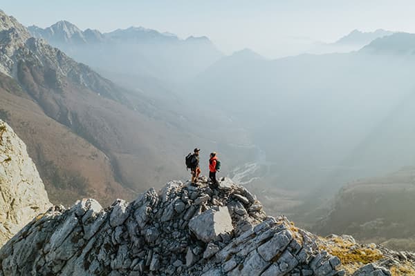 Thomas & Regina, from @edelweiss.on.the.road, are seen hiking the rugged peaks of Theth, Albania, surrounded by dramatic mountain views. This image captures a breathtaking moment during their vanlife adventure, exploring the remote and wild landscapes of the Albanian Alps.