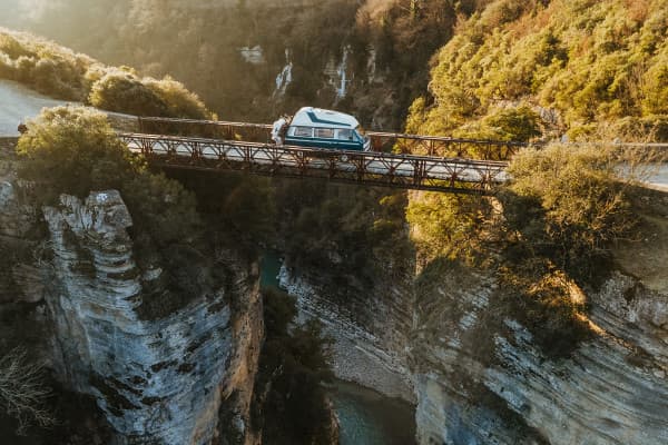 @edelweiss.on.the.road is captured crossing a narrow, iron bridge high above the steep cliffs of Osum Canyon in Albania. This stunning image showcases their VW T3 Vanagon "Edelweiss" amidst the dramatic, rugged beauty of the canyon, reflecting their adventurous vanlife journey through the breathtaking landscapes of the Balkans.