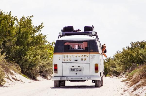 Rear view of Volkswagen T2 Kombi, adorned with stickers, traveling on a sandy road surrounded by greenery in Mexico, highlighting Belu and Lucho's (@viajayreite) journey from Argentina to Alaska.