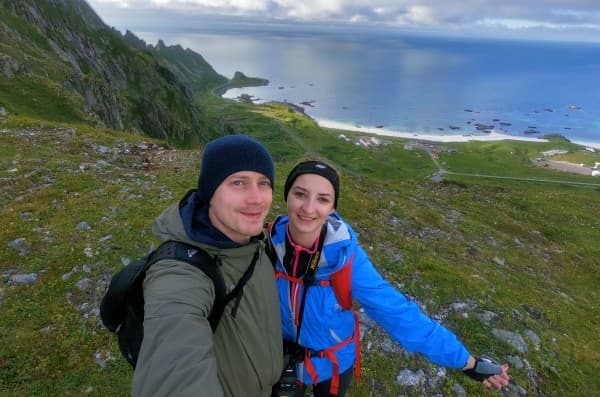 Mary & Peter exploring Norway - @travelvan 08/2021 Mary and Peter, from @travelvan, enjoying a hike with a breathtaking view of the coastline in Norway. The scenic landscape features green mountains and a clear blue sea.